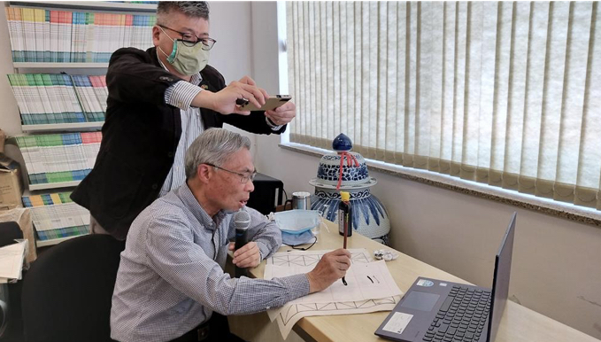 廖世秉老師(坐者)在鏡頭前示範楷書的寫法。