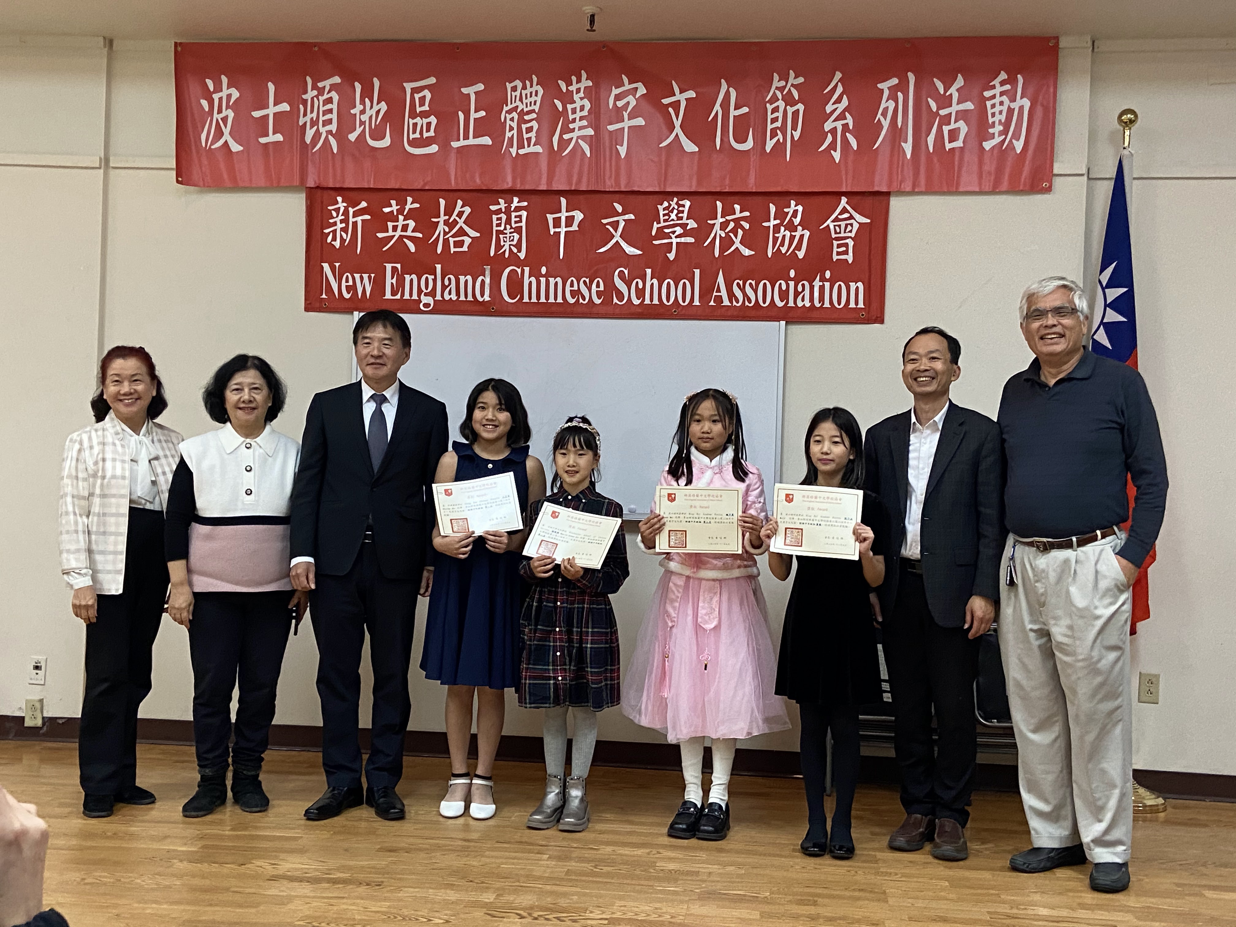 波士頓文教中心高家富主任 (左三)，新英格蘭中文學校協會會長黃冠群 (右二) ，朗誦評審吳萍萍老師(左一)，朗誦評審馮文鸞老師(左二)，朗誦評審莊紀華老師(右一)，及朗誦比賽中年級組得獎學生合影