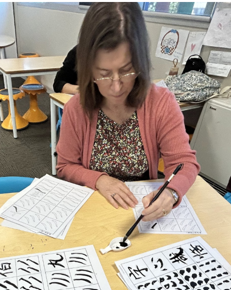 主流非華裔學員手執毛筆蘸墨，對照字帖認真練習楷書點畫結構，展現跨越文化的美學共鳴。 