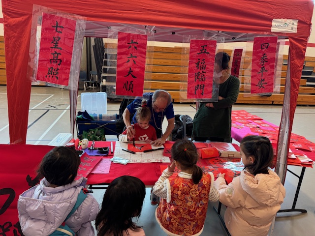 文化教學攤位之一是書法老師黃明嘉教小朋友拿毛筆寫春聯。