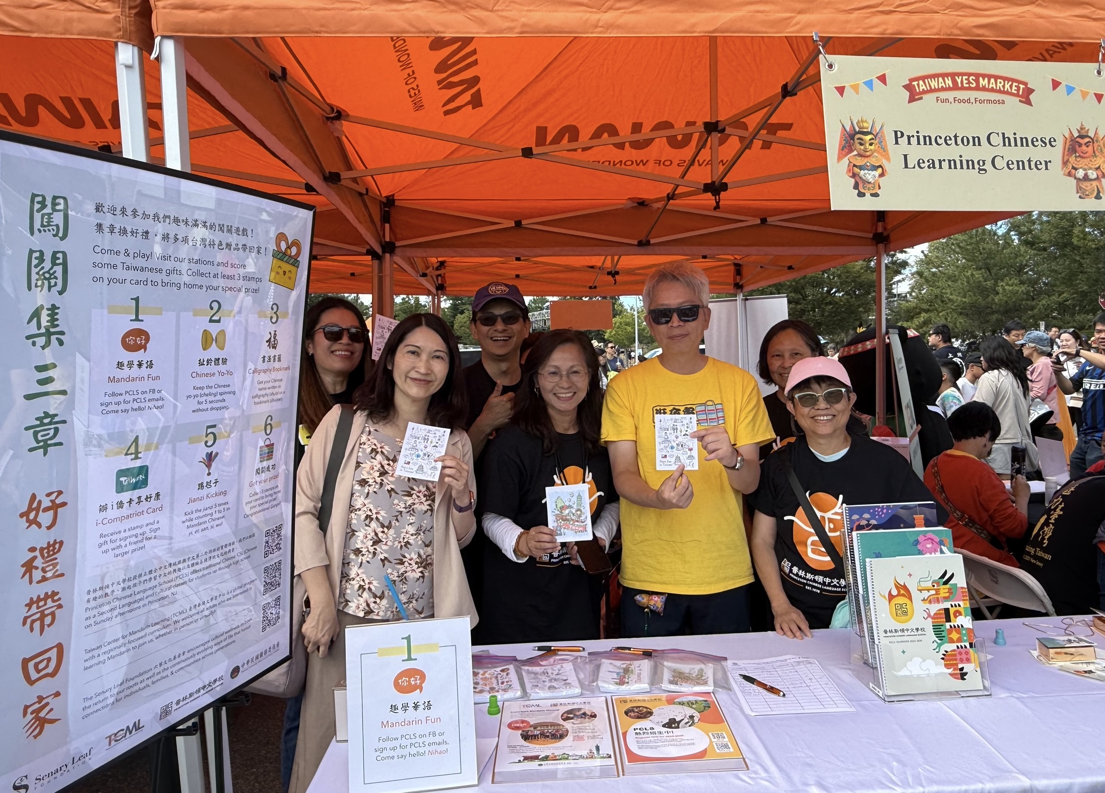 李志強大使(右二)及王怡如(左一)主任手持本校的客製化明信片，至攤位為義工們加油打氣