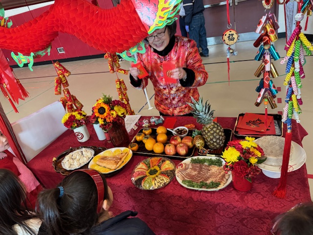 林梅英老師的過年應景食物的教學區，林老師準備了水餃（元寶）、魚（年年有餘）、蘋果（平平安安）、鳳梨（旺來）、柿子（事事如意）、和十錦菜（十全十美）等。