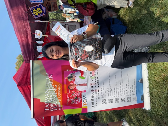 一位成人來賓對我們的**成人中文課程（TCML）**表現出極大興趣，開心地收到一件精美旗袍造型的贈品，象徵文化傳承與學習的開始。