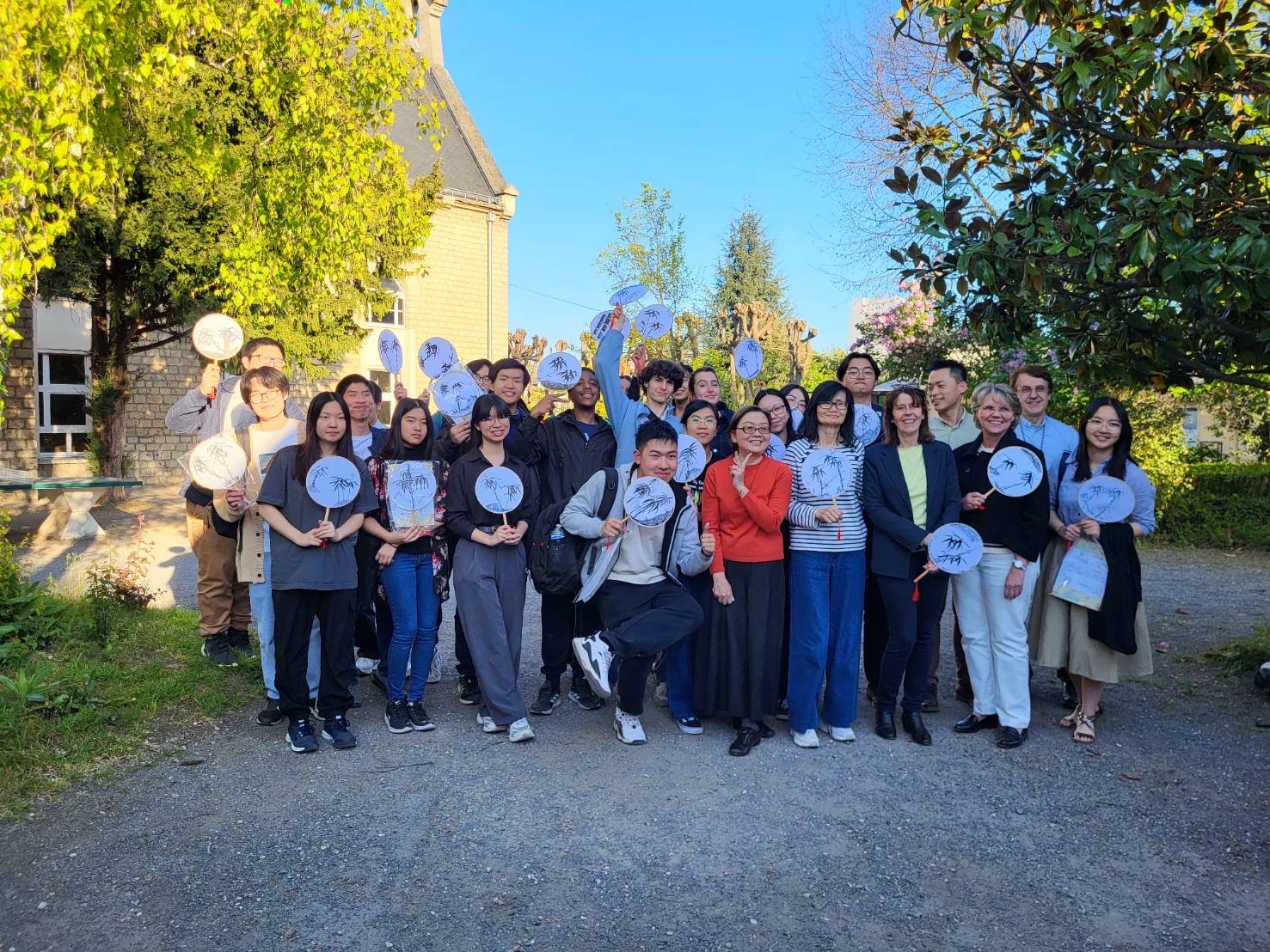 同學們和和他們的正副校長及貴賓們拿著完成的扇子，趁著美好春天在校園內合影