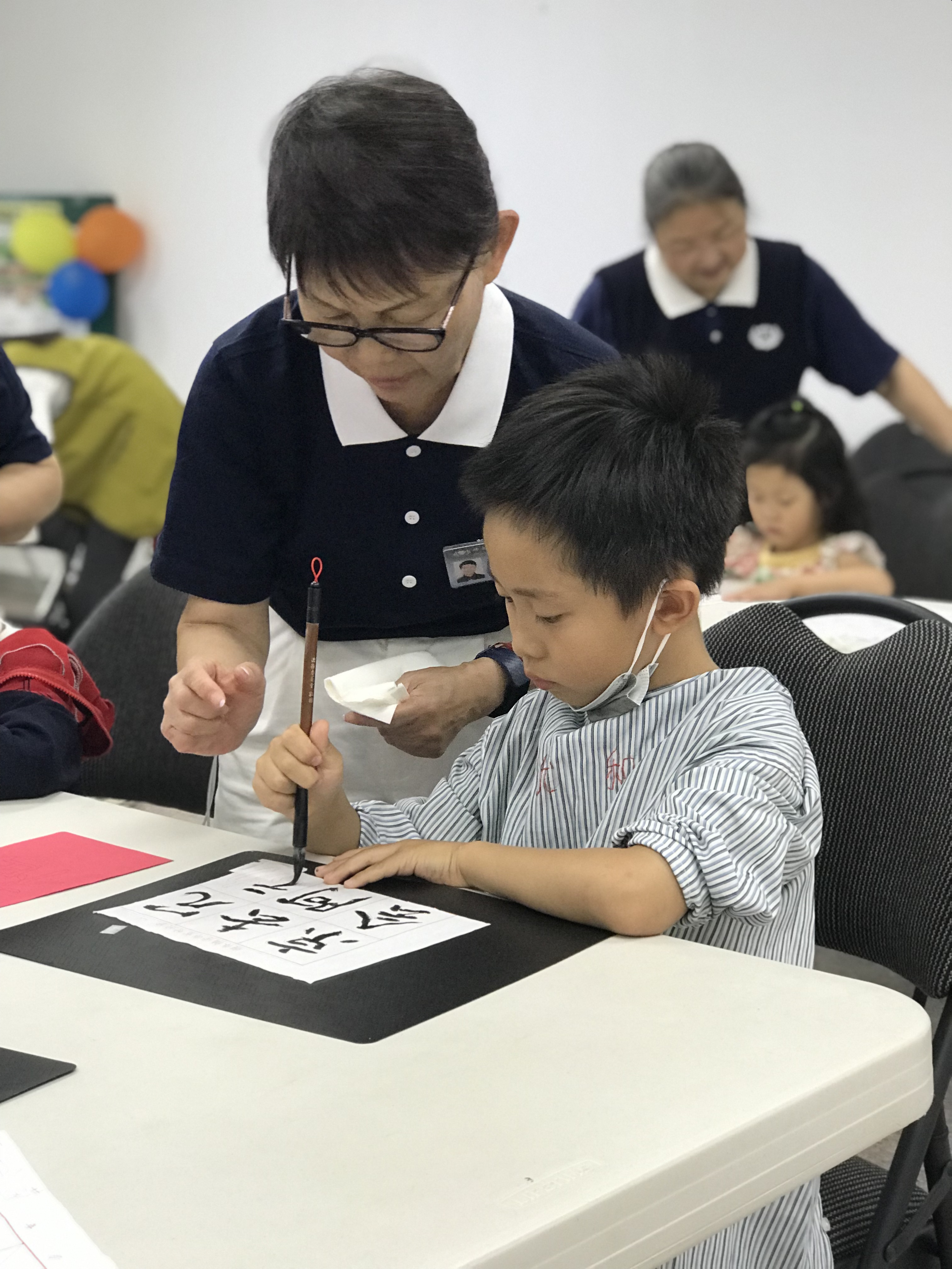 輔導老師耐心地教導小學員寫毛筆字